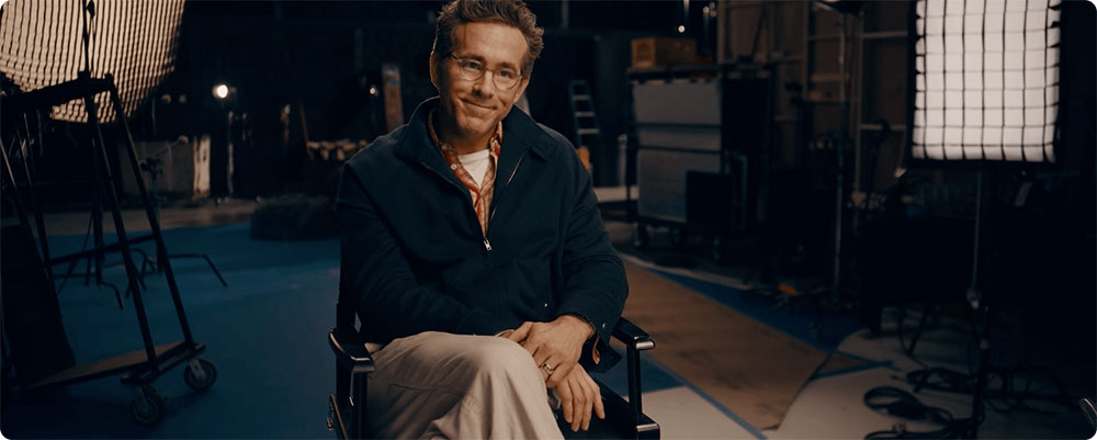 Ryan Reynolds sitting in director's chair on set smiling